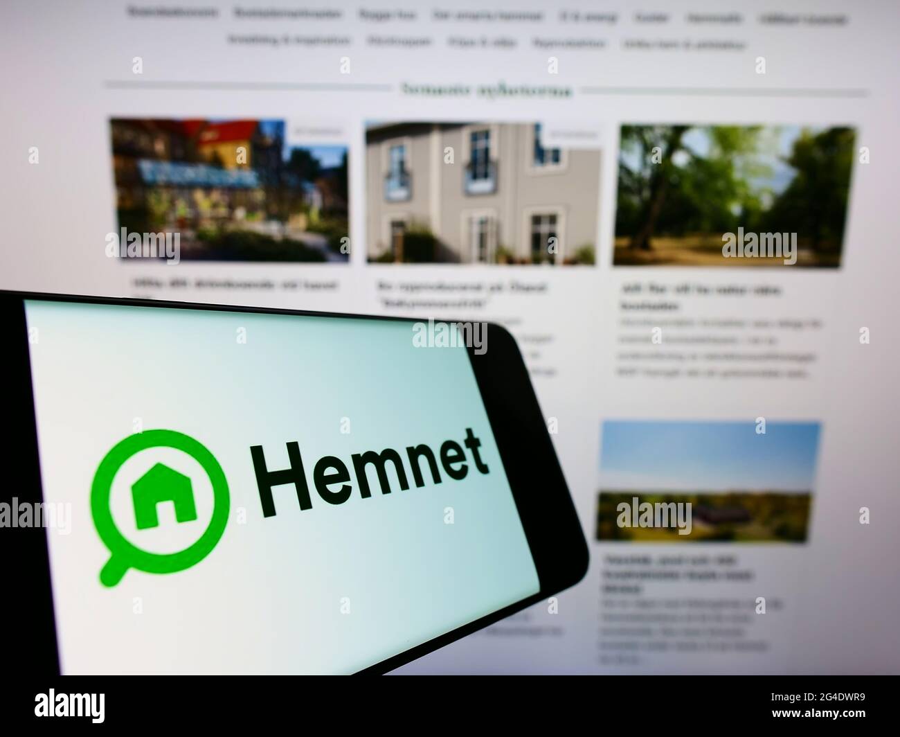 Mobile phone with logo of Swedish property platform company Hemnet AB on screen in front of business website. Focus on center-left of phone display. Stock Photo