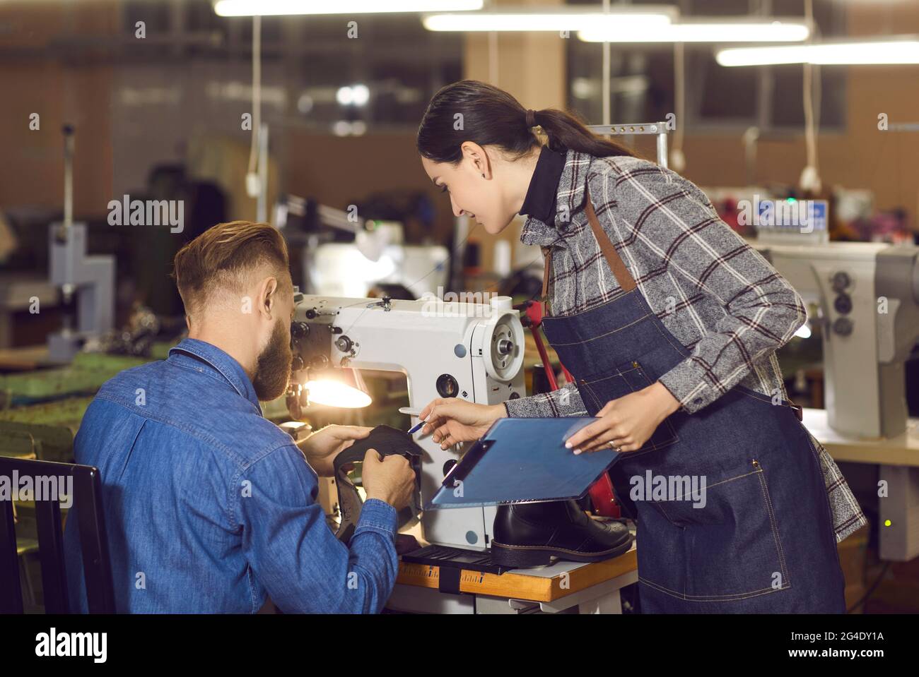 Female quality control manager talking to shoemaker working at workplace Stock Photo