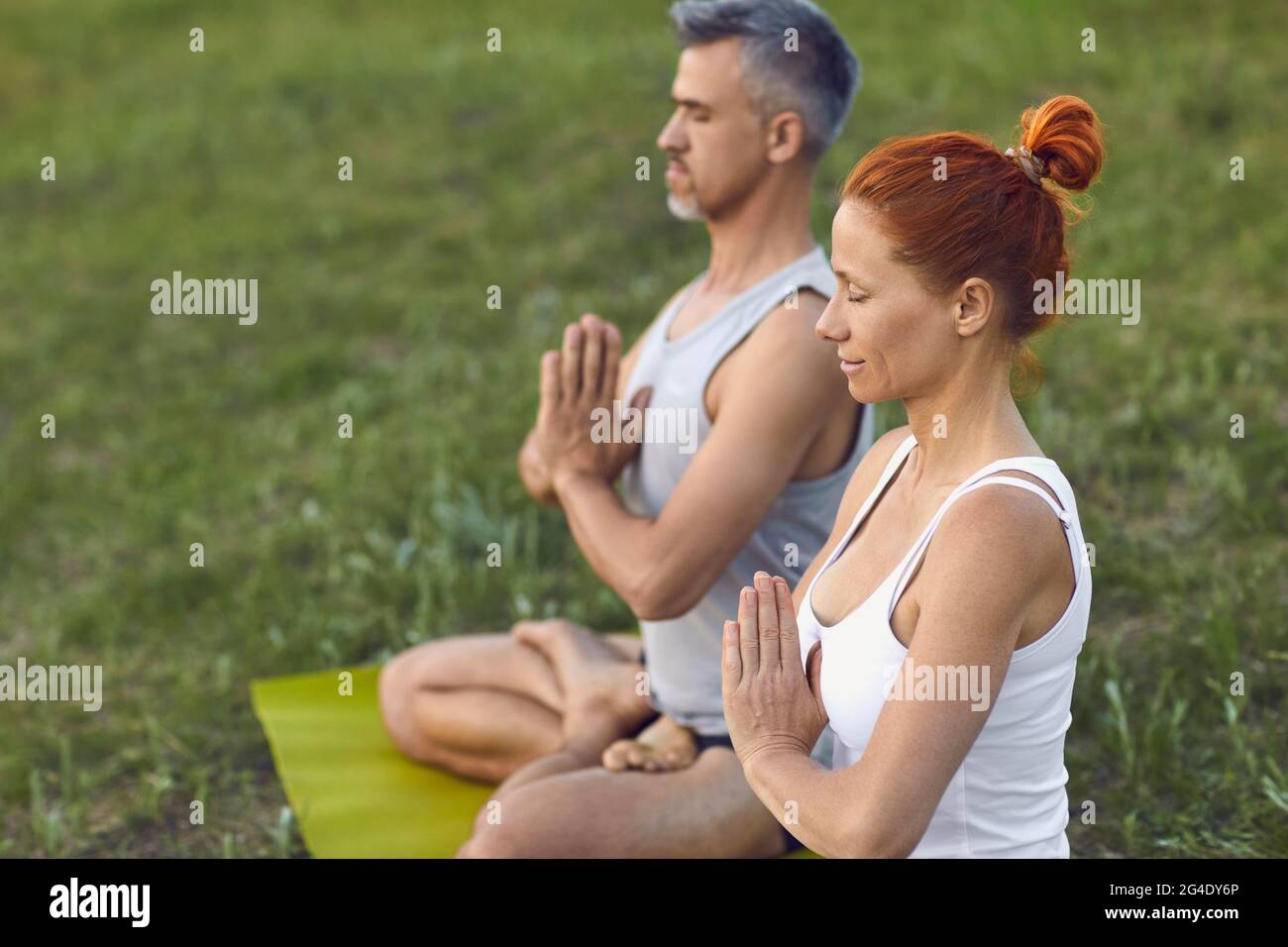 Woman and man sitting in lotus position with eyes closed, meditating and practicing yoga on nature Stock Photo