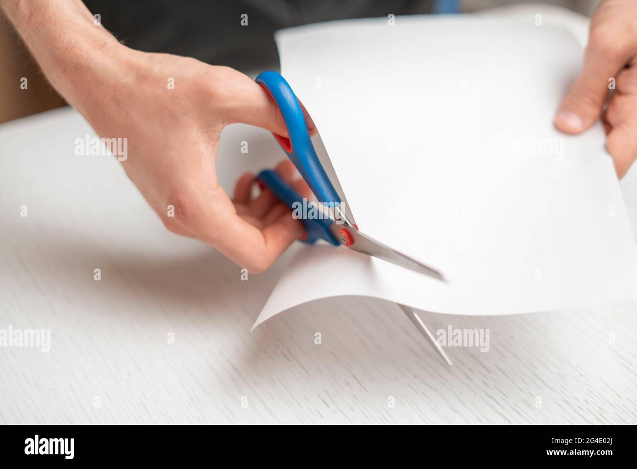 person's hands holding piece of paper sheet and cut it with scissors Stock Photo Alamy