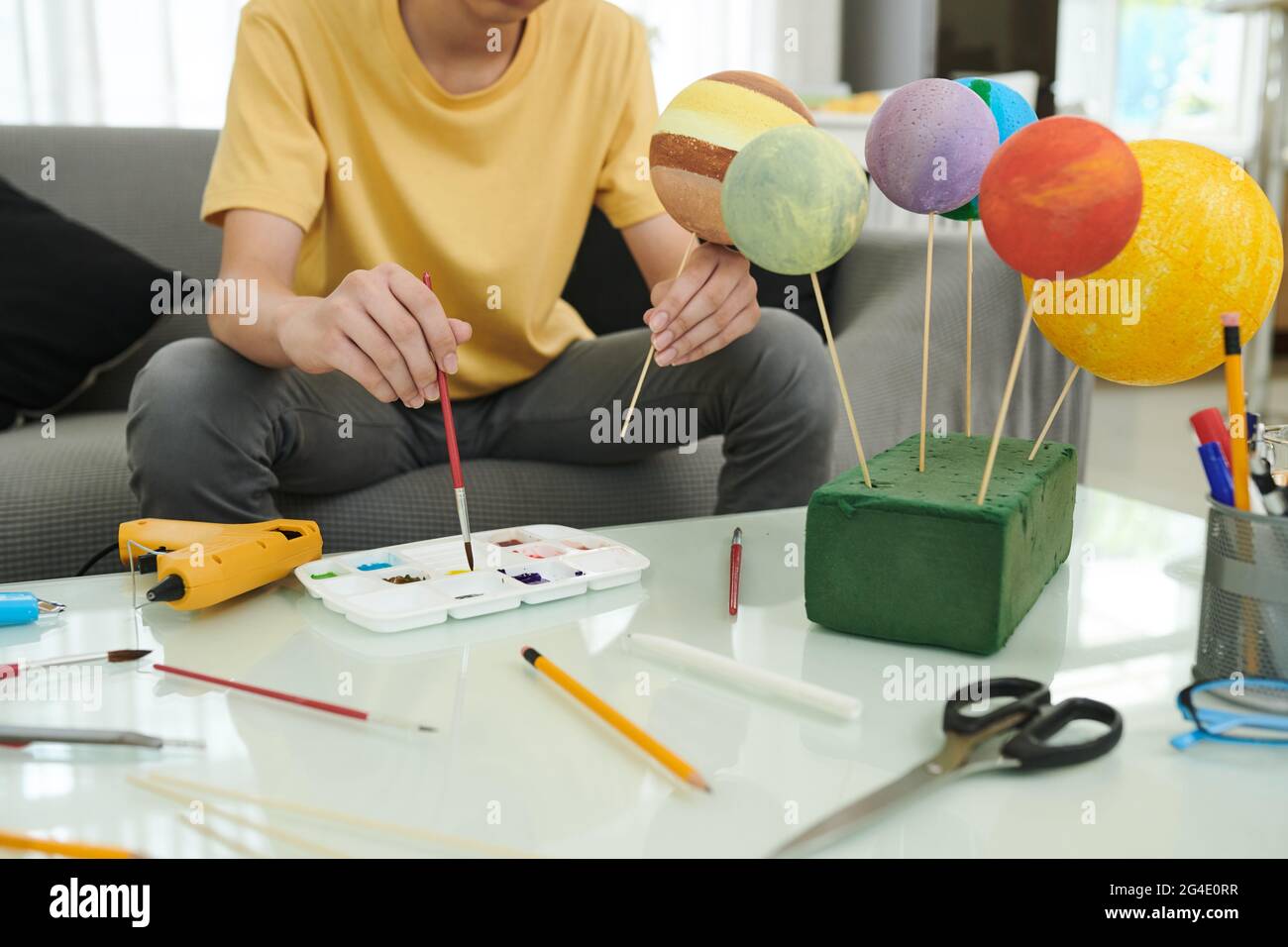Teenage boy painting styrofoam balls when making model of Solar System for school Stock Photo