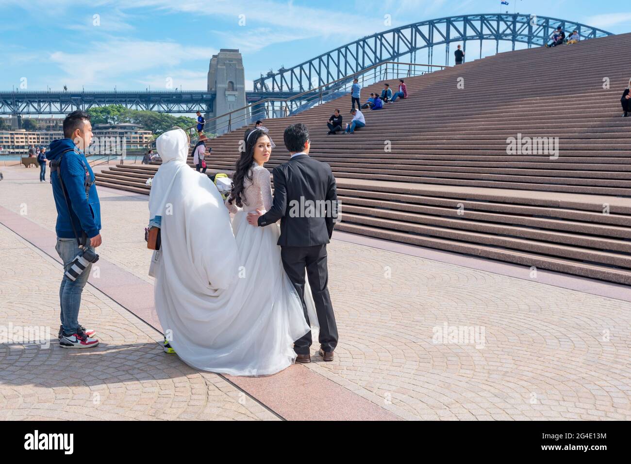 A bride and groom at the Sydney Opera House and Sydney Harbour in Australia waits with their photographer before climbing the front steps Stock Photo