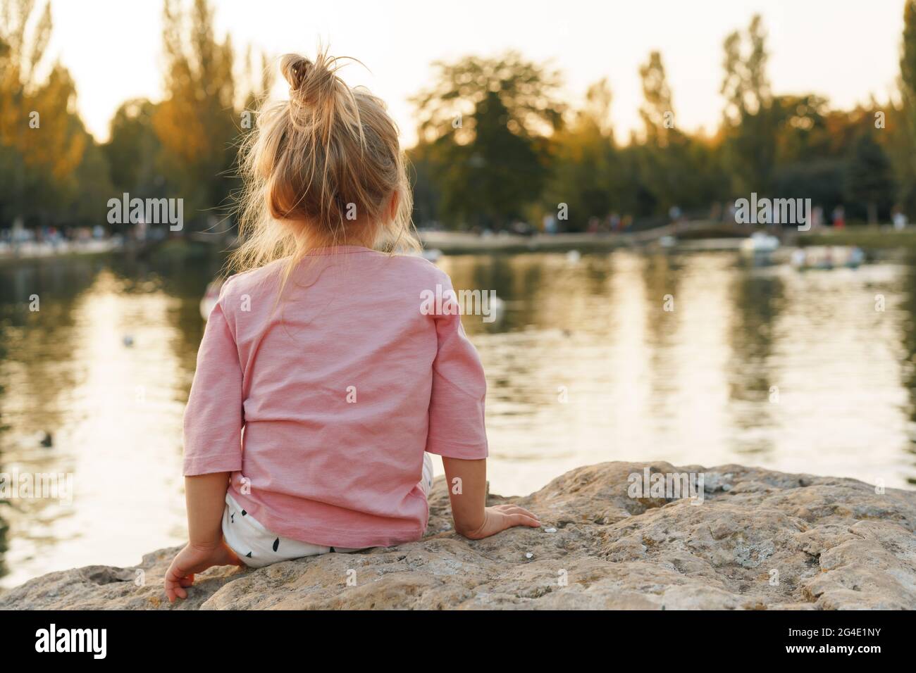 Little girl sitting on a huge stone in park near the lake Stock Photo ...