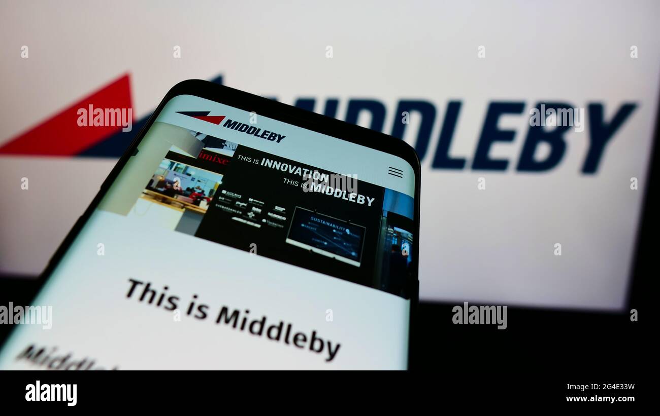 Smartphone with website of US cooking equipment company Middleby Corporation on screen in front of business logo. Focus on top-left of phone display. Stock Photo