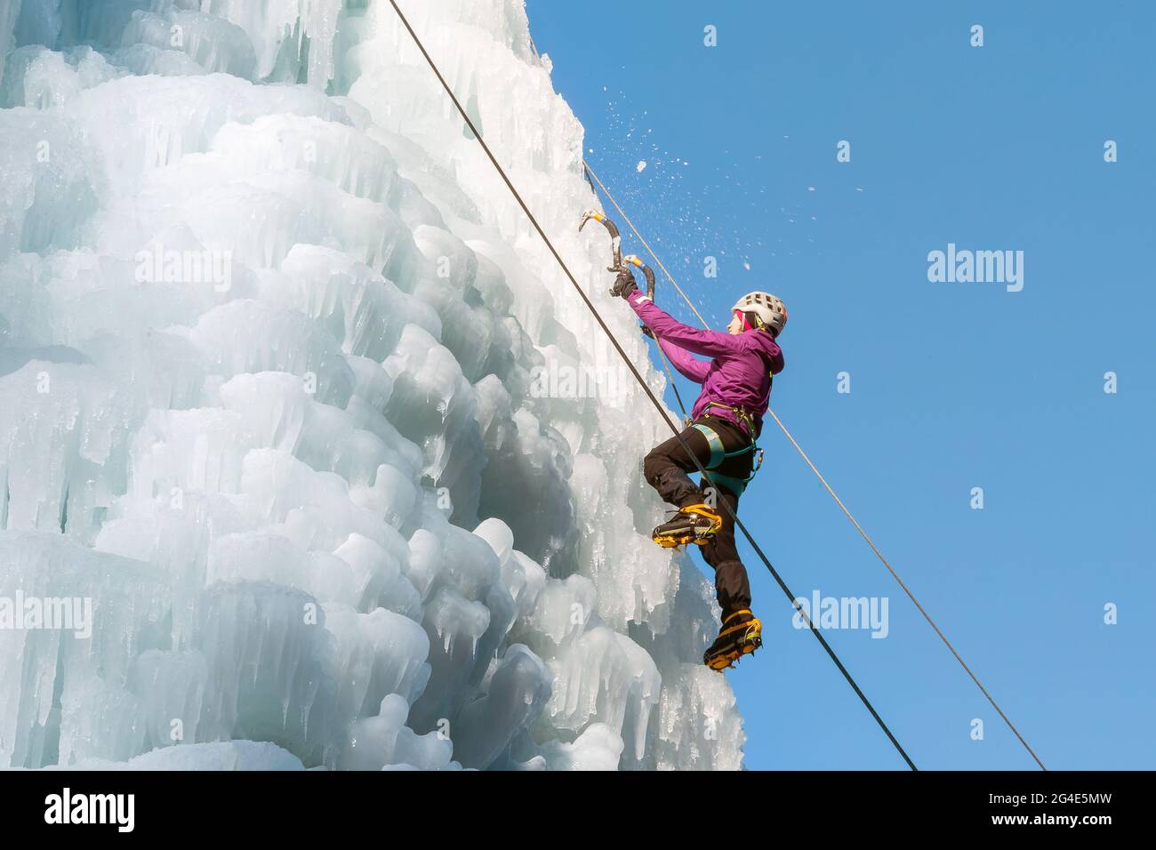 Female ice climber hiking a frozen waterfall, pushing axe pick into the slope and moving up to the top Stock Photo