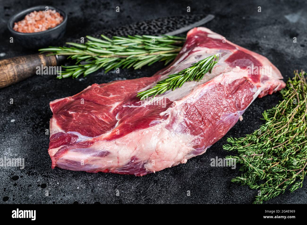 Fresh Raw lamb or goat shoulder meat with butcher knife. Black background. Top view Stock Photo