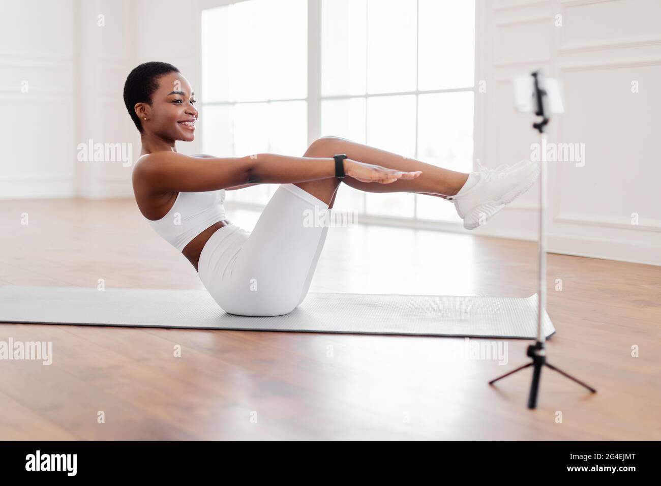 Smiling Black Woman Doing Sit-ups Exercise Looking At Phone Stock Photo