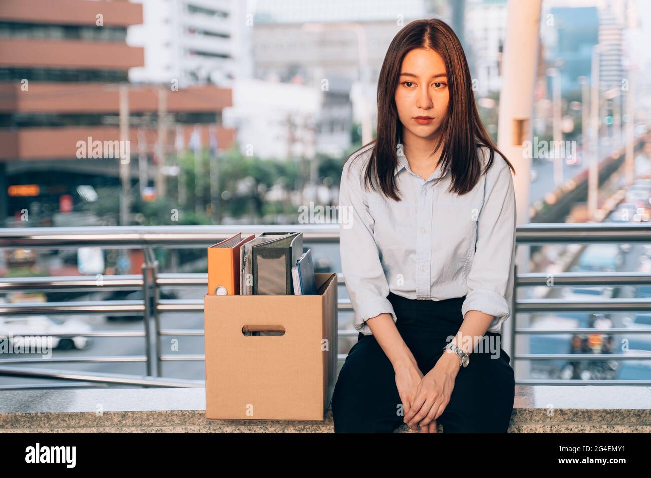 Stressed and worried young Asian woman with box of items sitting alone after being laid off from job due to recession and economic stress in industry Stock Photo