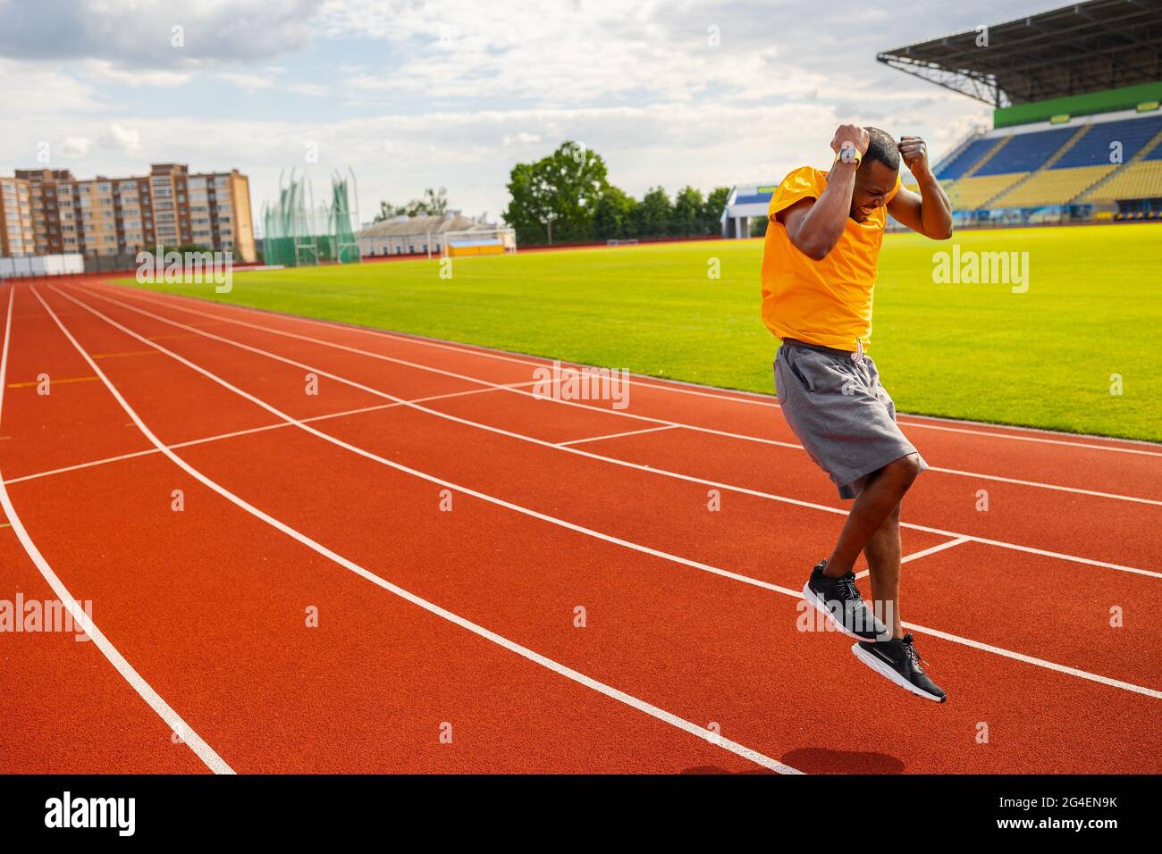 Joyful Afro American runner in yellow sportswear happily jumping and winning the runner competition, receiving first place, training and working hard Stock Photo