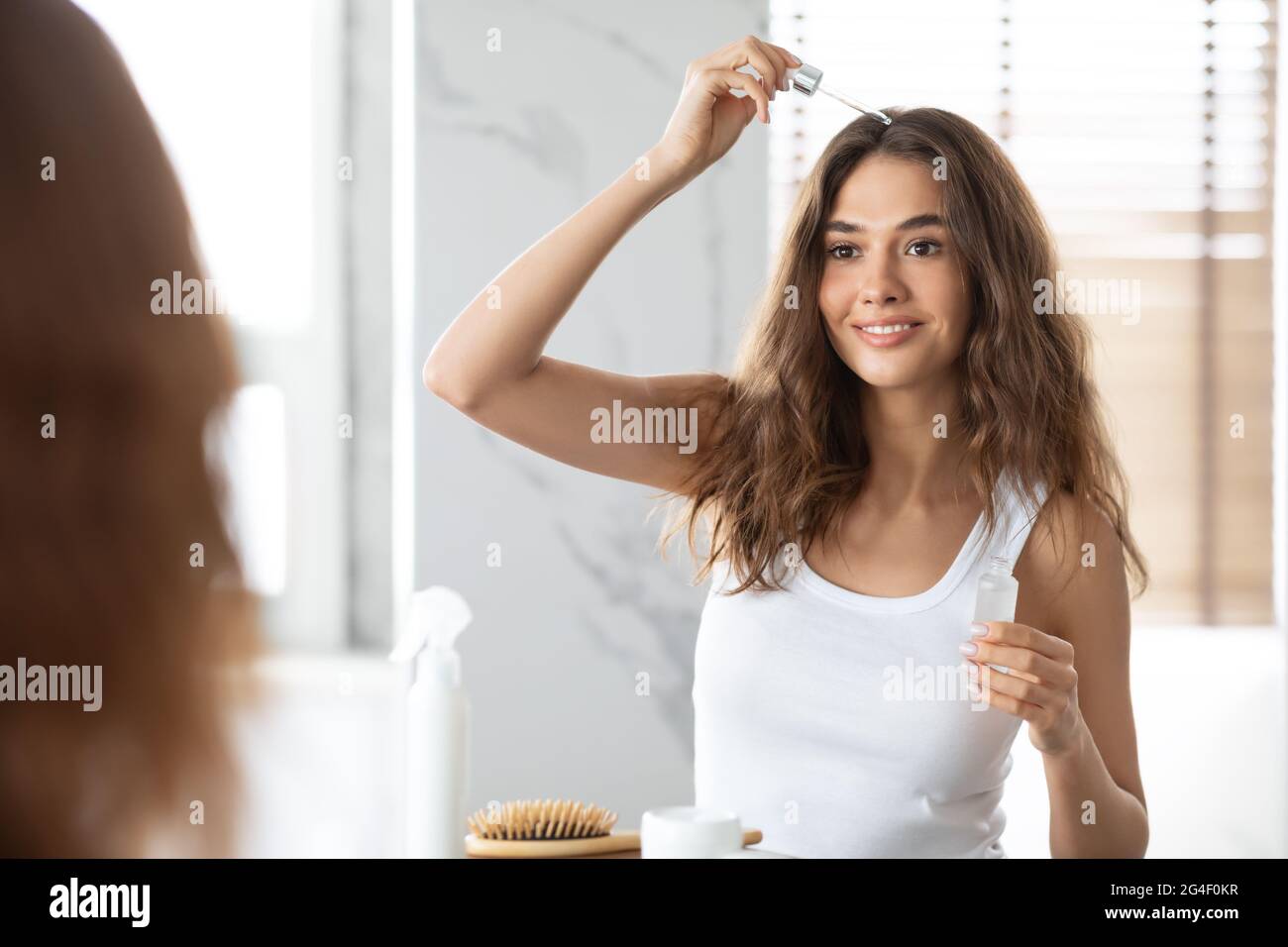 Woman Applying Serum For Hair Repair In Bathroom Stock Photo