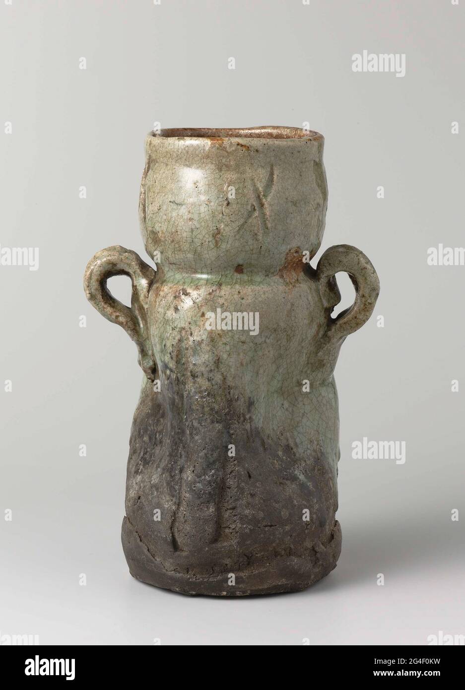 . Vase of stoneware with two ears on the shoulder, partly covered with a celadongin glaze. The belly is dented and four times a rubbing cross on the neck. The lower part of the vase is unglazed. Old dealer label on the bottom with 'N.V. Hammer - Far Eastern Art New York / 440 '. I go. Stock Photo