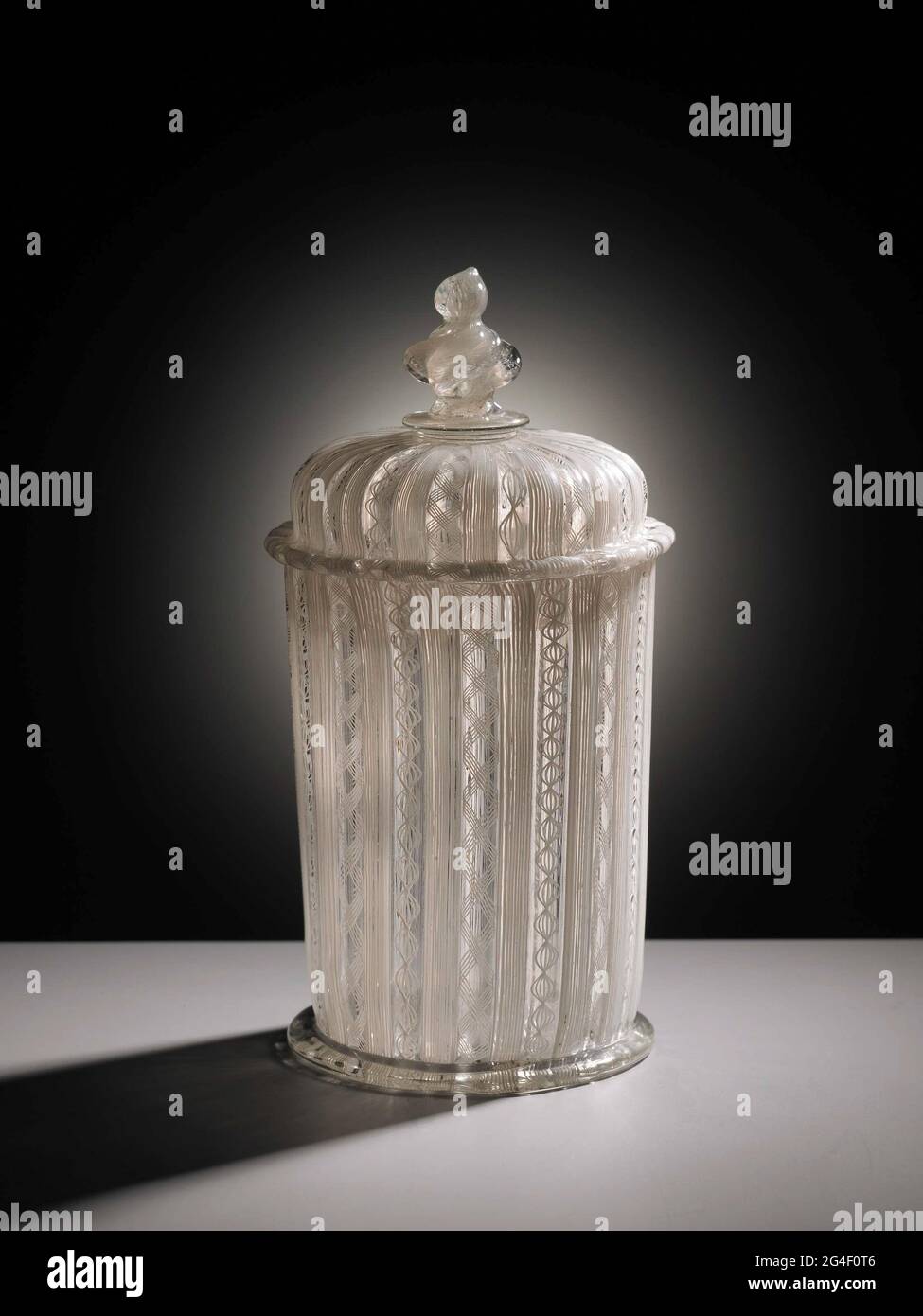 . Cup with lid on flat stand ring. Cylindrical body with a flat bottom. Vaulted lid with overrunning edge and teared button with one disc. Body, lid and button of filigraanglas a fili and a retortoli, straight ring and colorless glass disk Stock Photo