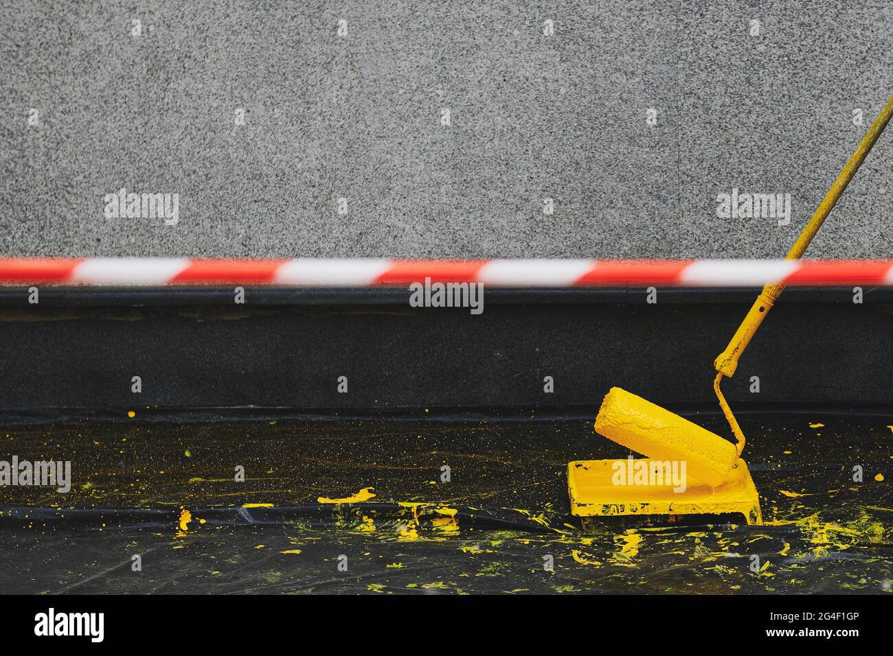 Signal tape beside painting the building. Paint roller in a paint tray near a grey wall. Painting the wall in yellow colour. Black plastic cover on th Stock Photo