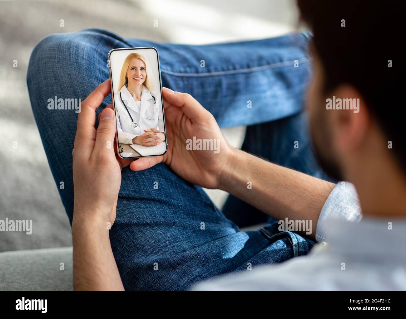 Unrecognizable man using cellphone at home, talking to doctor Stock Photo