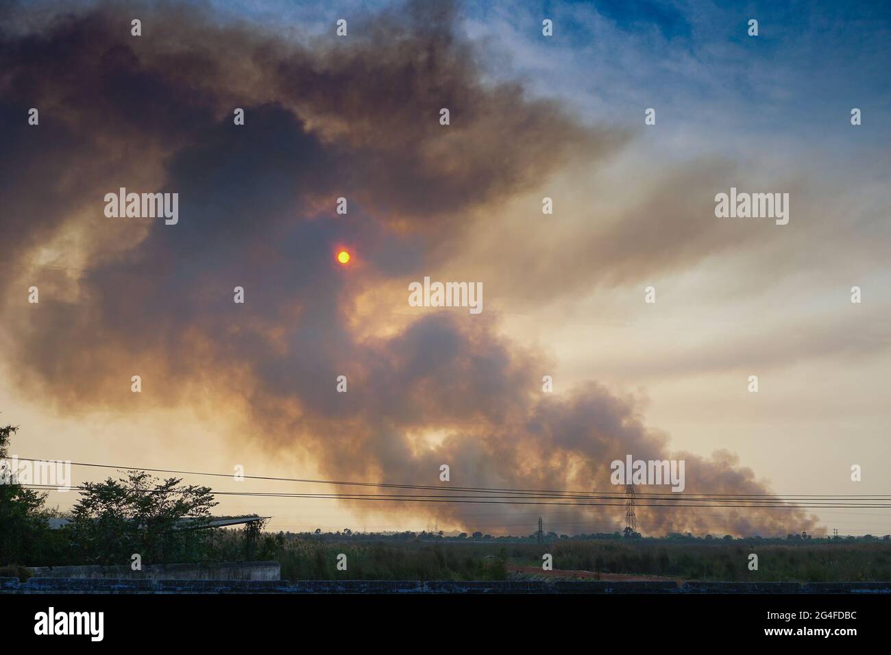 Smoke coming out of factories in the horizon, air pollution is spreading like clouds and covering the setting sun. Shot at rural village of WB, India. Stock Photo