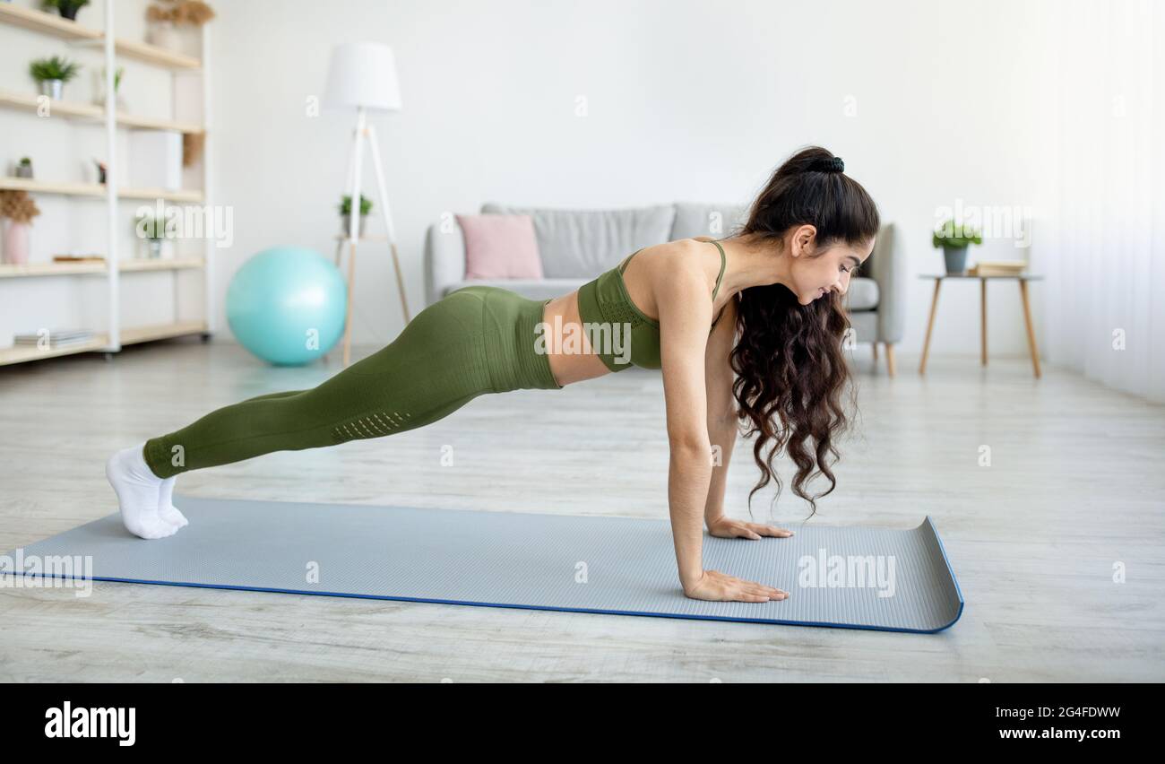 Side View Of Millennial Indian Woman Standing In Plank Pose On Yoga Mat