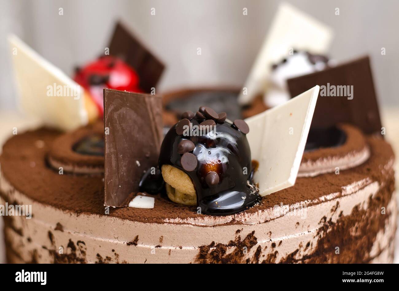 Decorating a chocolate cake close-up, with a ball poured with chocolate with slices of black and white chocolate Stock Photo