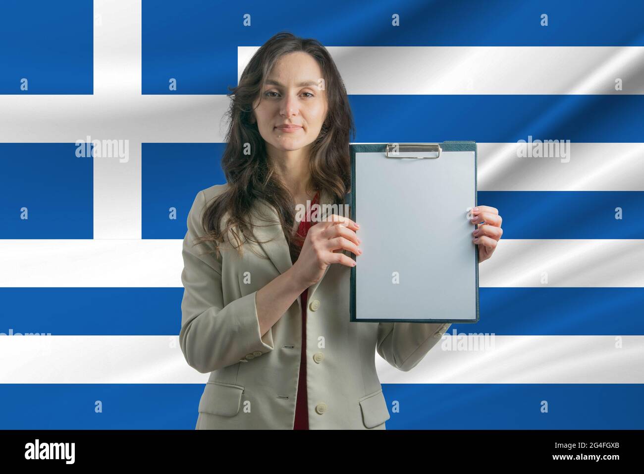 Study in Greece. Beautiful woman holding a sheet of paper in her hands. Girl on the background of the flag of Greece. Stock Photo
