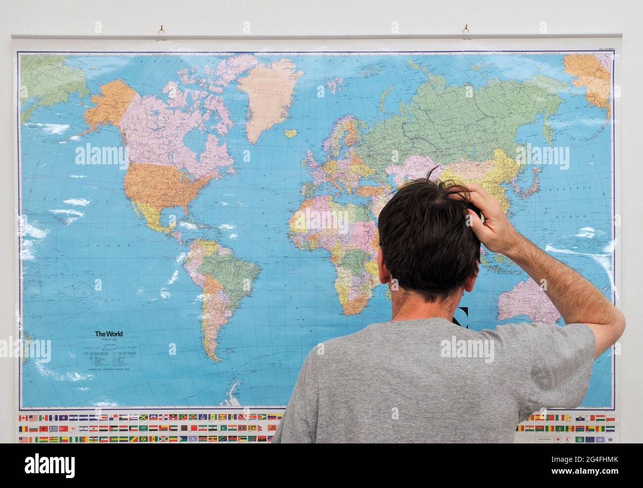 young adult man looking at world map with hand on his head Stock Photo