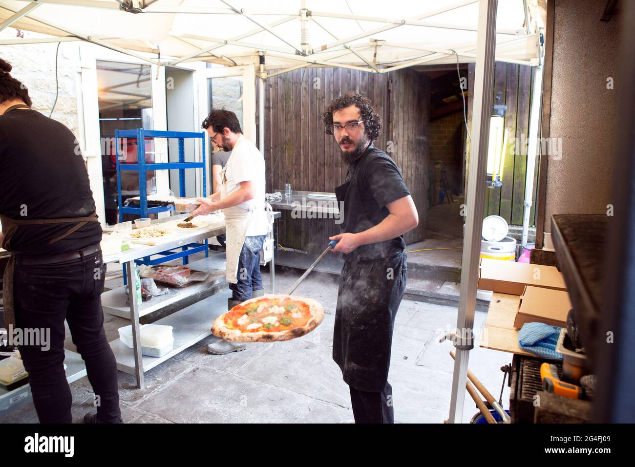 Coronavirus stories from the food industry. Staff member Josh Al-Kazhraji removes a pizza from the outdoorwood-ovens at The Moorcock Inn (owned by Aim Stock Photo