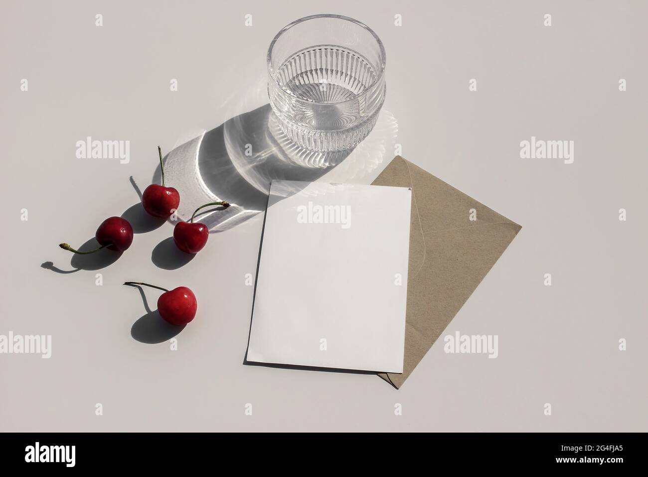 Summer food still life composition. Red cherries fruit on beige table background. Stationery mock up scene. Blank greeting card, invitation, glass of Stock Photo