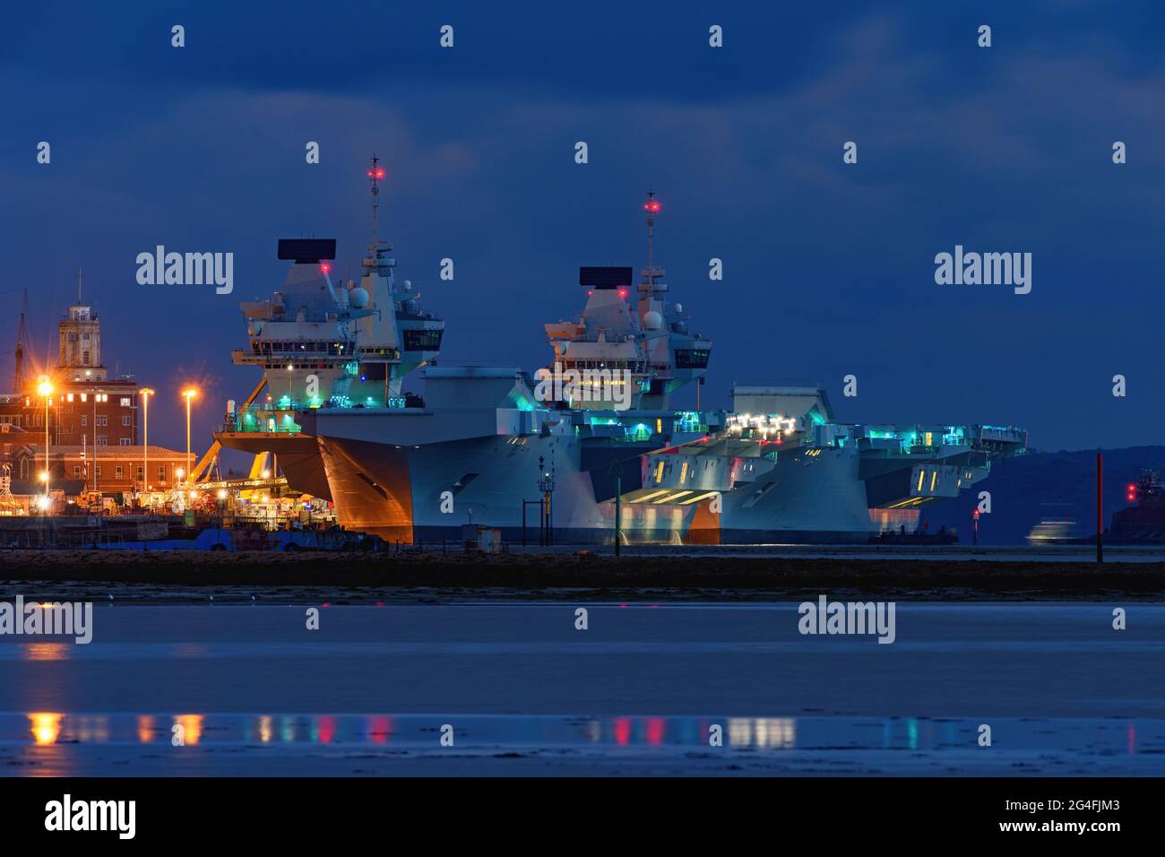 A night view of the Royal Navy aircraft carriers HMS Queen Elizabeth and HMS Prince of Wales together alongside HM naval base in Portsmouth Harbour - Stock Photo