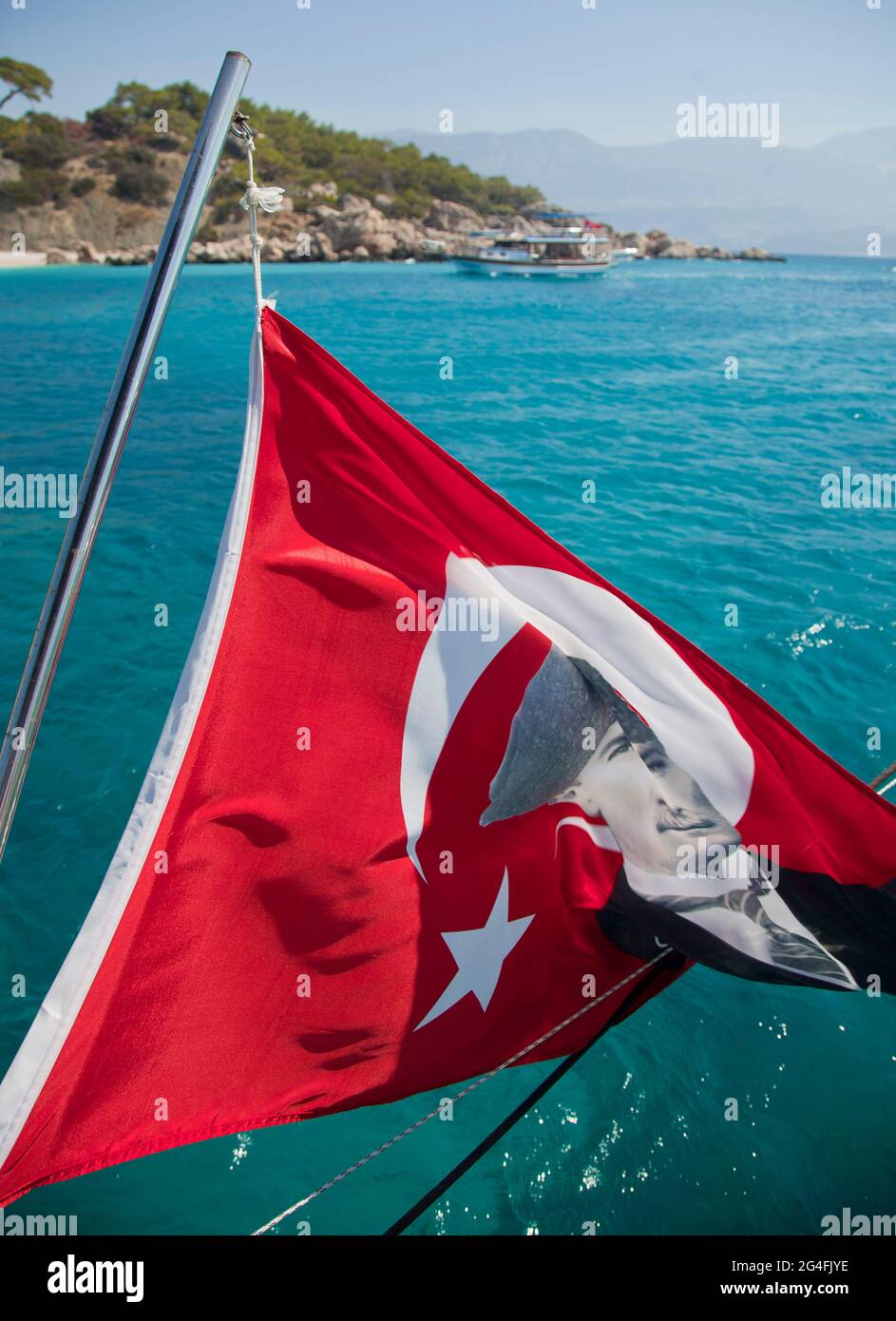 A Turkish flag with the image of Mustafa Kemal Atatürk flies from the rear of a Gullet boat anchored in a bay near to Kalkan in Turkey.  Kalkan is a p Stock Photo