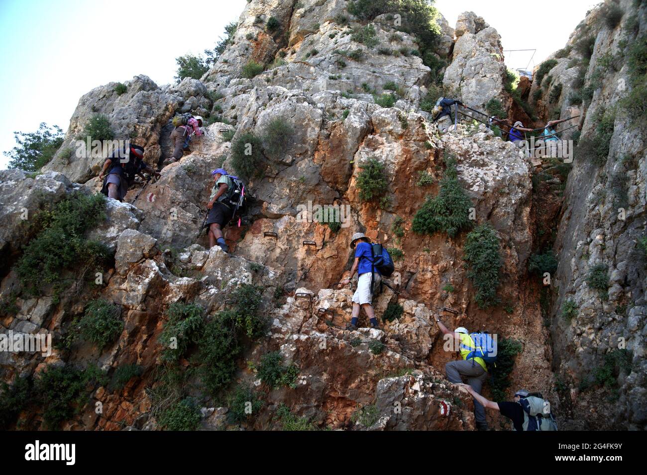 Hikers, senior adults in their 50s, 60s and 70s, active seniors, use hand holds and a steel cable to go up a rock to Mount Arbel above Sea of Galelee Stock Photo