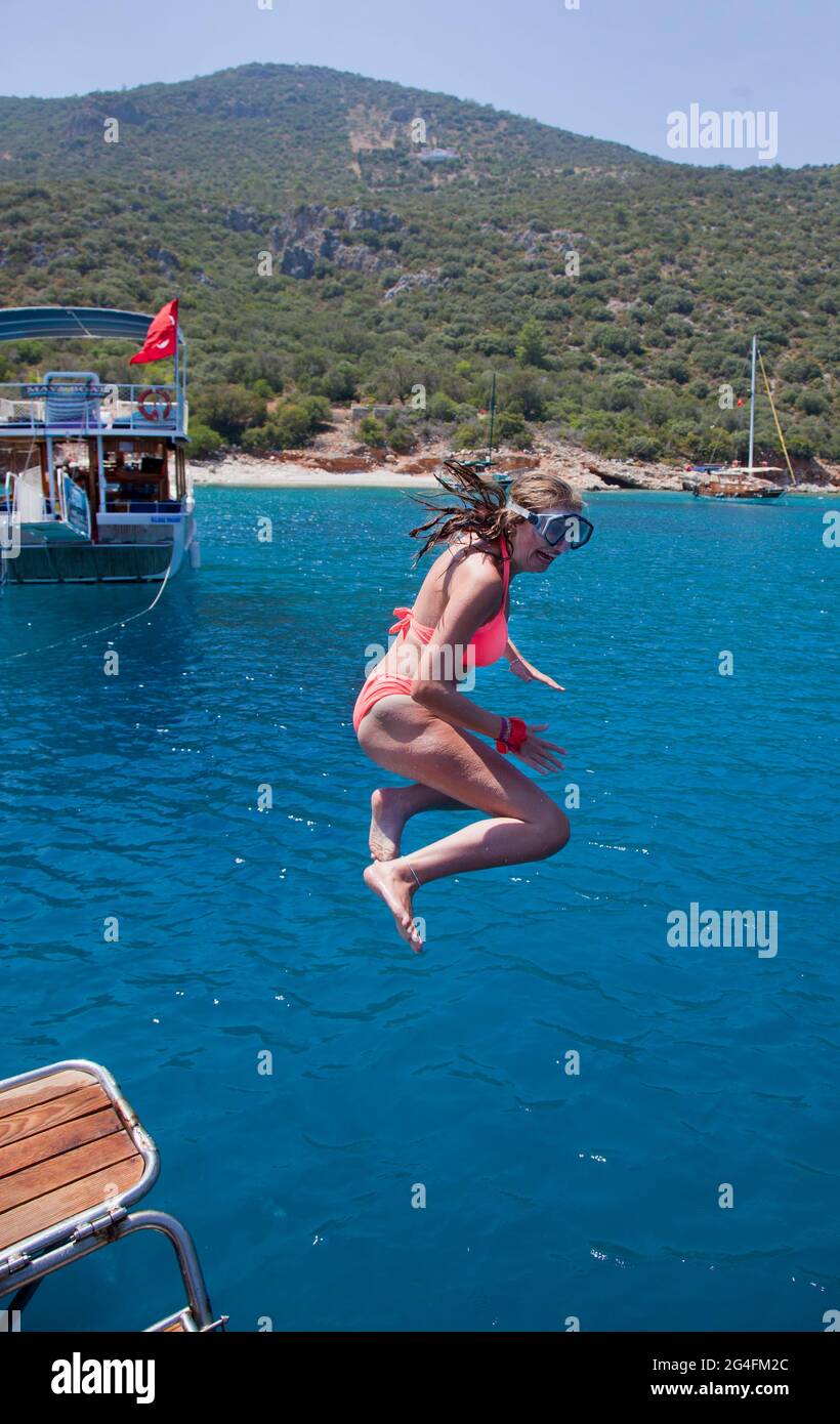 Kalkan, Turkey, 2020. A young lady leaps from a charter yacht moored in a sheltered part of Kalkan bay in Turkey;  located on the Turkish Mediterranea Stock Photo