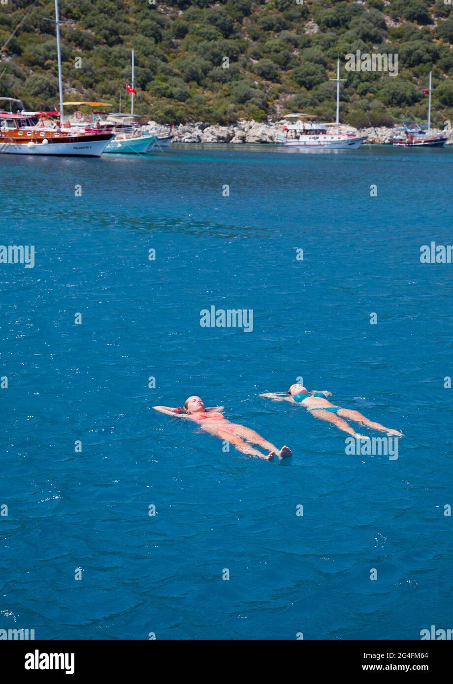 Kalkan, Turkey, 2020. two young ladies floating in the sea near to moored charter yachts in a sheltered part of Kalkan bay in Turkey;  located on the Stock Photo