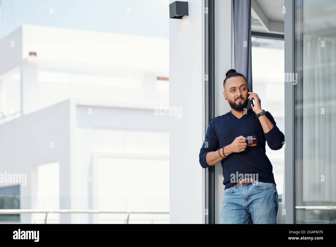 Pensive handsome bearded man drinking tea and talking on phone with friend or colleague Stock Photo