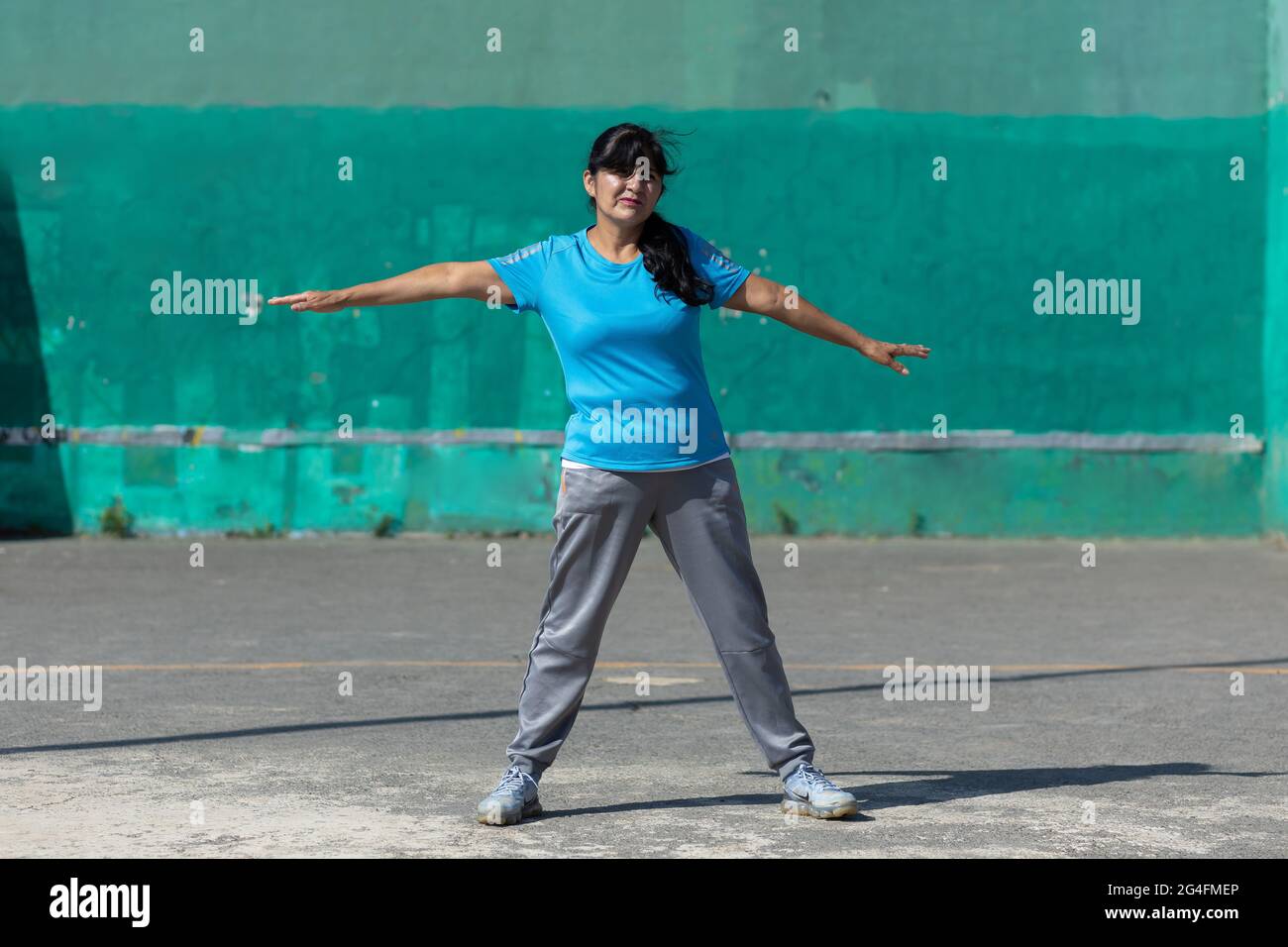 Mexican woman stretching with arms outspread; exercising outdoors Stock Photo
