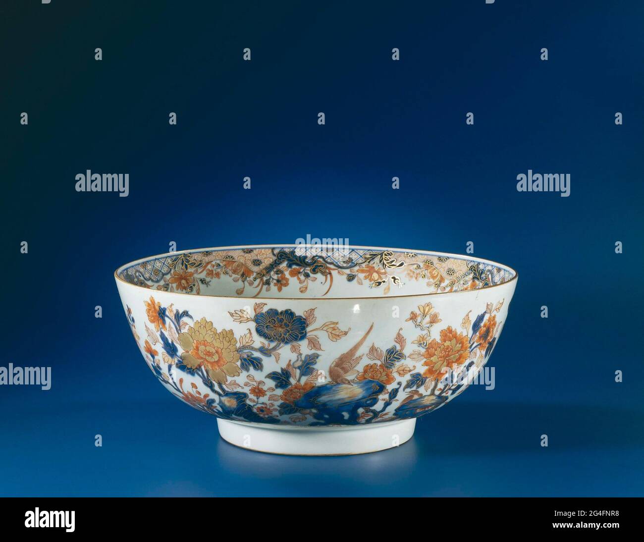 . Punch bowl of porcelain, painted in underglaze blue and on the glaze red and gold. On the outside wall a rock with two pheasants and a large flower group with peony and Magnolia, in addition a smaller peony plant, orchid and loose flower branch above which a butterfly; four carp on the bottom; The inner edge with cartouches with napkin interspersed with opened painting rolling with cloud motif and flowers; below dependent flowers. Chinese Imari. Stock Photo
