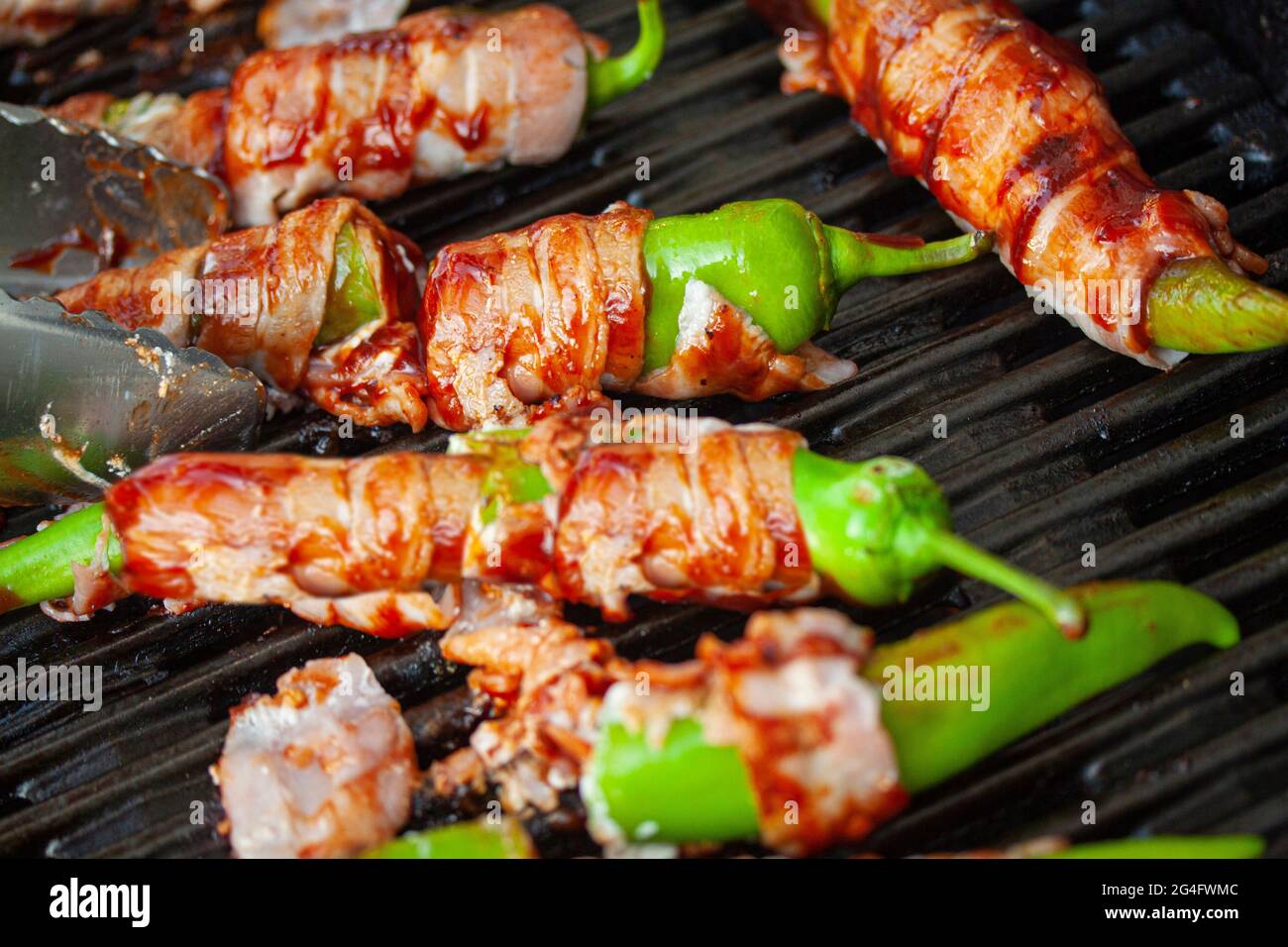 Jalapeno poppers on burning, grill. Spicy peppers stuffed with cream cheese and wrapped in bacon. Top view with selective focus. Stock Photo