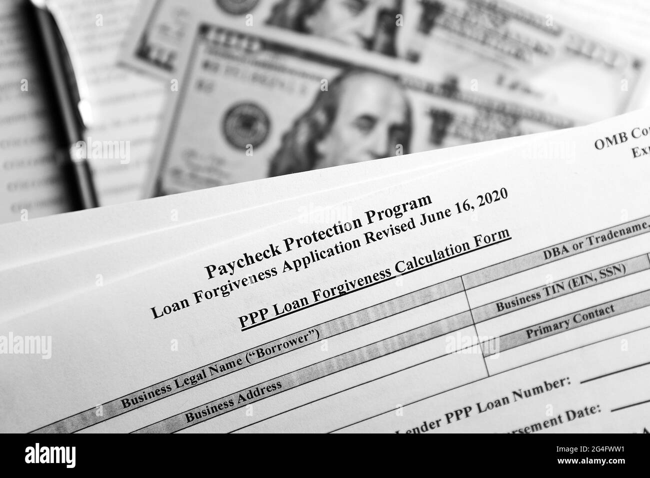 selective focus monochrome photo of paycheck protection program loan forgiveness application form revised, on a background of dollar bills and a pen Stock Photo