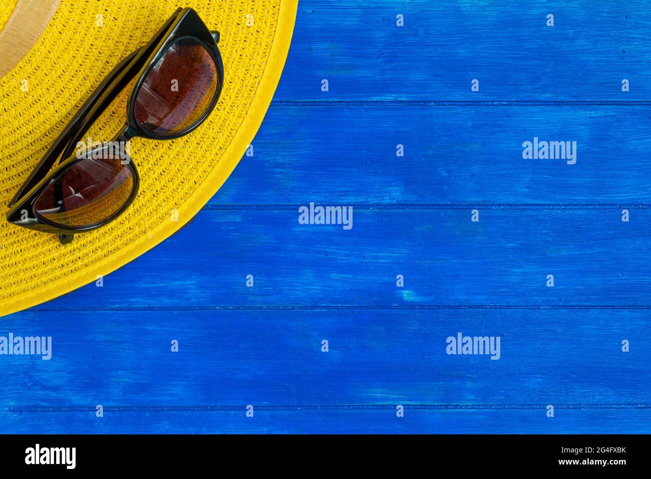 Top view of yellow summer hat and sunglasses on blue wooden background ...