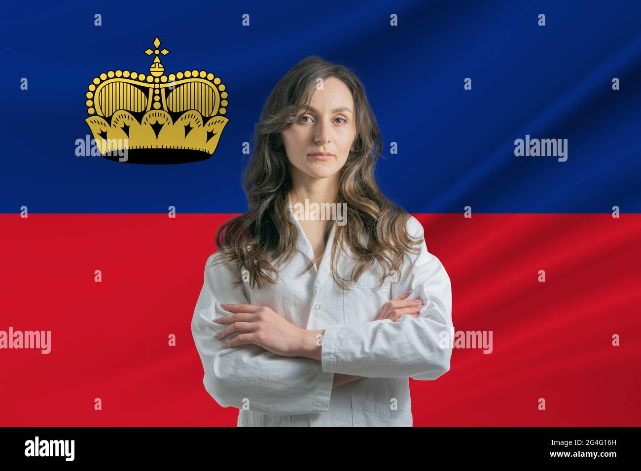 Medicine in Liechtenstein. Happy beautiful female doctor in medical coat standing with crossed arms against the background of the flag of Liechtenstei Stock Photo