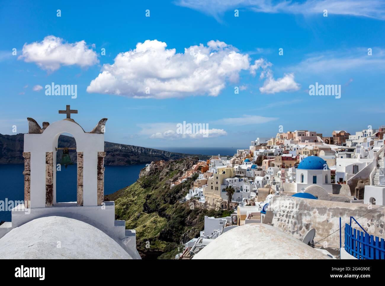Santorini island, Greece. White orthodox church bells Oia town, caldera cityscape, blue cloudy sky, calm sea. Greek island Cyclades, summer travel des Stock Photo