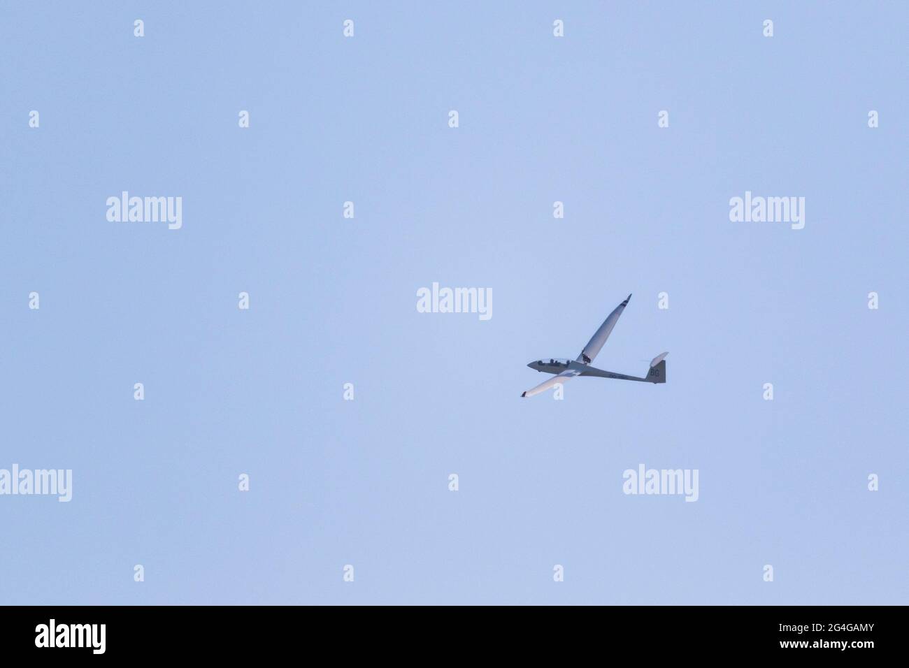 A portrait of a glider plane flying in the distance in a light blue sky