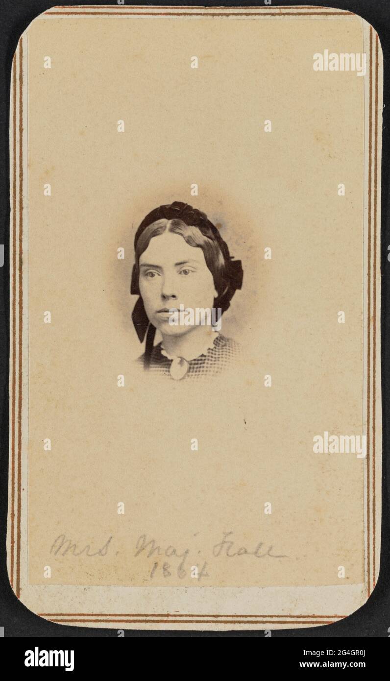 Carte-de-visite of Maria Miller Woodhull Hall photographed in bust portrait. Her face is turned one quarter to her right and she looks off camera. She is wearing a black cap with ruffled or ribbon details on the back of her head and a plaid dress with a large oval brooch at her front neck. Hall's head is at the center of the print, with the background behind it fading at the edges in the popular style of the time. There is a double-lined border printed in gold ink surrounding the outside edges of the card mount.;Handwritten in graphite at the bottom of the photograph is the text &quot;Mrs. Maj Stock Photo