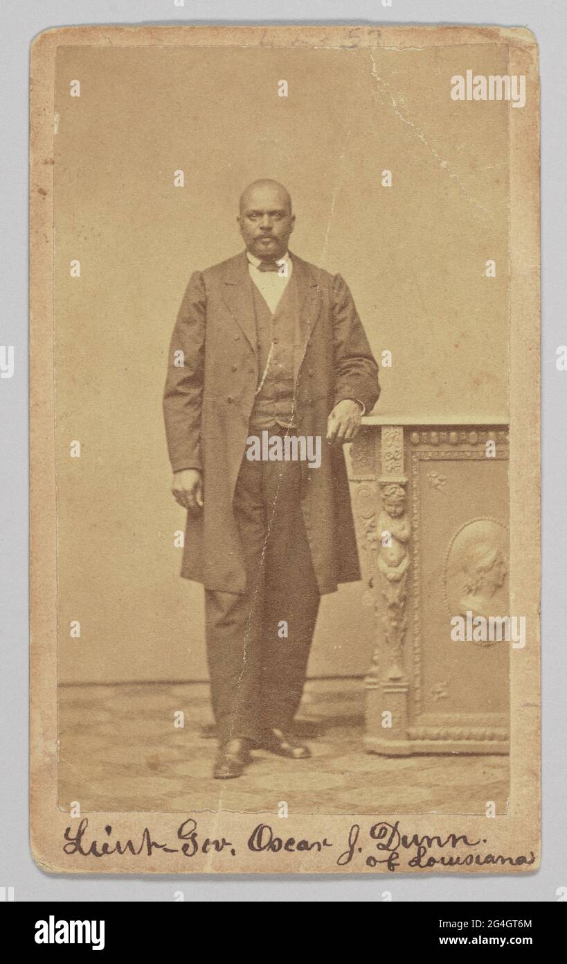 An albumen print carte-de-visite portrait of African-American politician, musician and businessman Oscar J. Dunn. He is photographed standing with his right foot slightly forward than his left and has his left arm resting on a pedestal. He is wearing a dark colored suit, vest and a bowtie. A watch chain is visible on the right side of his vest. He is looking directly at the camera. The photograph is inscribed on at the top and bottom of the front. At the bottom, handwritten in black ink, is: [Lieut Gov. Oscar J. Dunn / of Louisiana]. Stock Photo