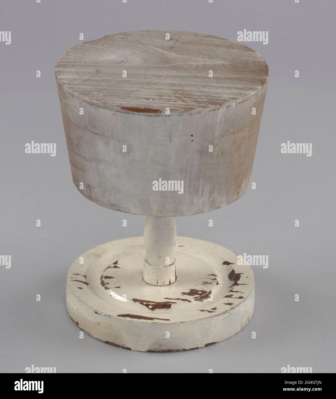 A wooden hat stand base (a) and form (b) painted white. The base is circular with one groove carved into the top of the base. A turned wooden dowel is screwed into the center of the base. The form is circular and tapers in toward the bottom where it attaches to the stand via a hole in the center of the underside. Mae Reeves (1912-2016) was a pioneering African-American milliner who was famous for her custom-made hats. Her business, Mae's Millinery Shop in downtown Philadelphia, was one of the first shops in the city to be owned by a woman of African American heritage. Stock Photo