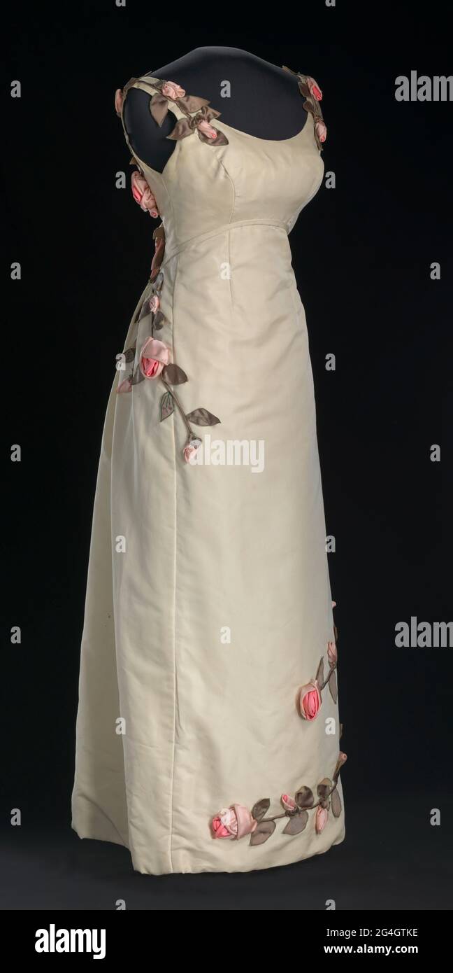 An ivory dress decorated with swirls of handmade fabric rose vines,  designed by Ann Lowe. The variety of rose depicted on the dress is the  American Beauty, which has led to it