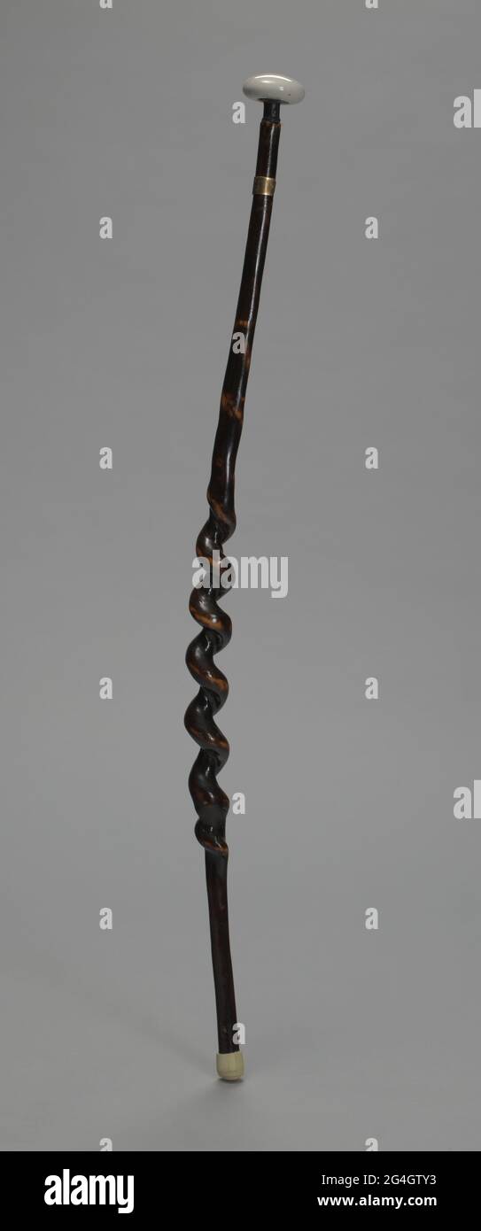 A cane, or walking stick, used by Chief Master Carl Brashear (1931-2006), an African-American United States Navy sailor and master diver, despite having his left leg amputated in 1966. The body of the cane is alternating black and brown in color, with a shiny surface. The middle portion of the cane is twisted, creating a twirling appearance. The handle of the cane is white, and resembles a door knob. At the bottom of the cane, there is a white stopper. There is a gold tag with text etched into it, reading: [BILL COPELIN / SONORA. KY / '97] circling around the cane, close to the top, underneath Stock Photo