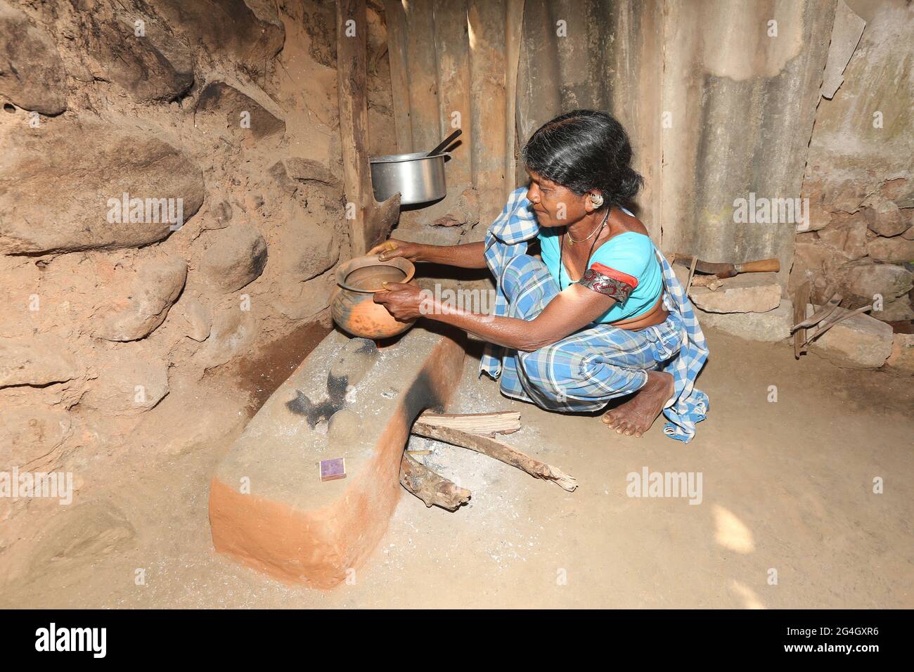 LANJIA SAORA TRIBE. Tribal woman making Ragi food using mud pot and traditional mud hearth in kitchen. Puttasingh village in Odisha, India Stock Photo