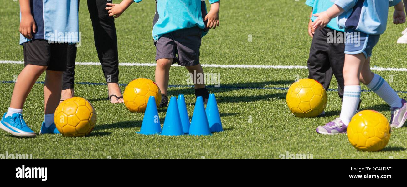 Preschool children learning ho to play soccer with yellow balls and blue cones. Stock Photo