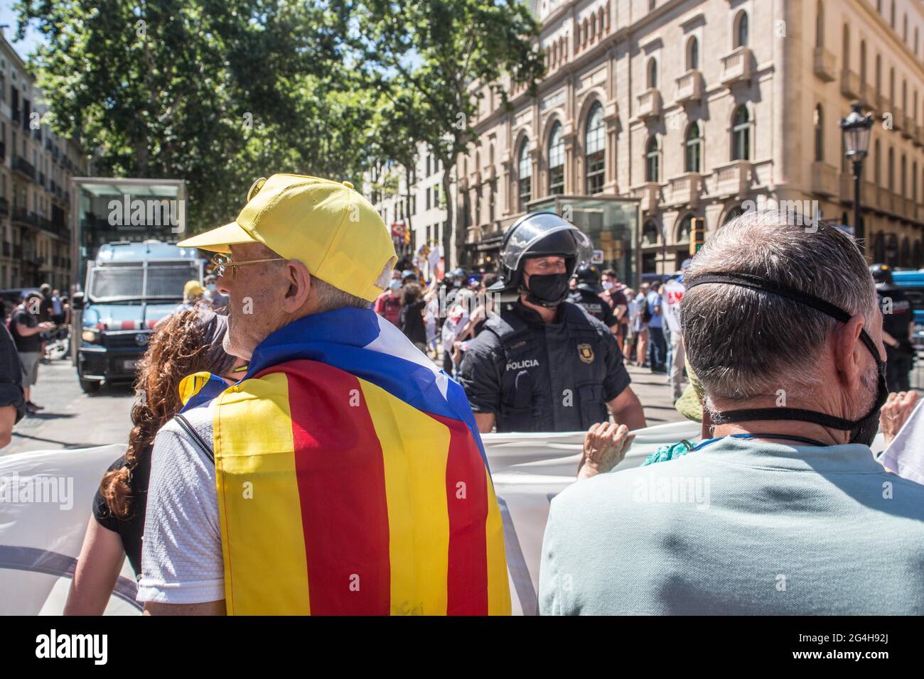 A protester seen with the Catalan independence flag on his back in front of the police during the demonstration.Hundreds of Catalan independentistas have demonstrated in Las Ramblas in Barcelona, in front of the Gran Teatre del Liceu (Great Theater of the Lyceum), shielded by many policemen, to protest the visit of the President of the Spanish Government, Pedro Sanchez, who has held a conference entitled 'Reunion: a project for the future for all of Spain', with the expectation of an imminent granting of pardons for the independence leaders in prison. The protesters protested to denounce that Stock Photo