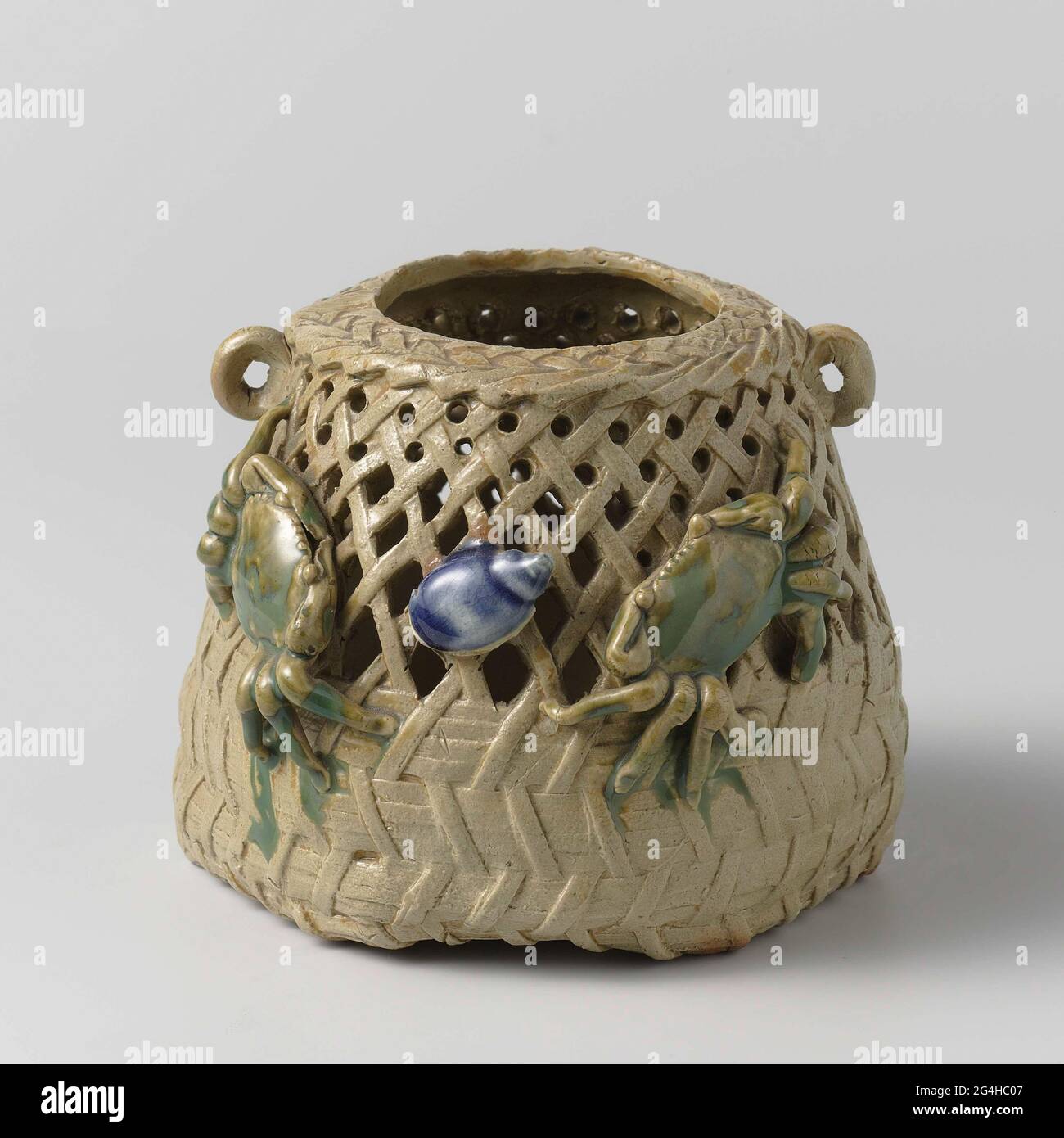 . Pot of stoneware in the shape of a basket with openwork wall and two small, raised ears, painted on the glaze in blue and green. Two modeled crabs and a shell on the outside wall. Six holes in the soil. Stock Photo