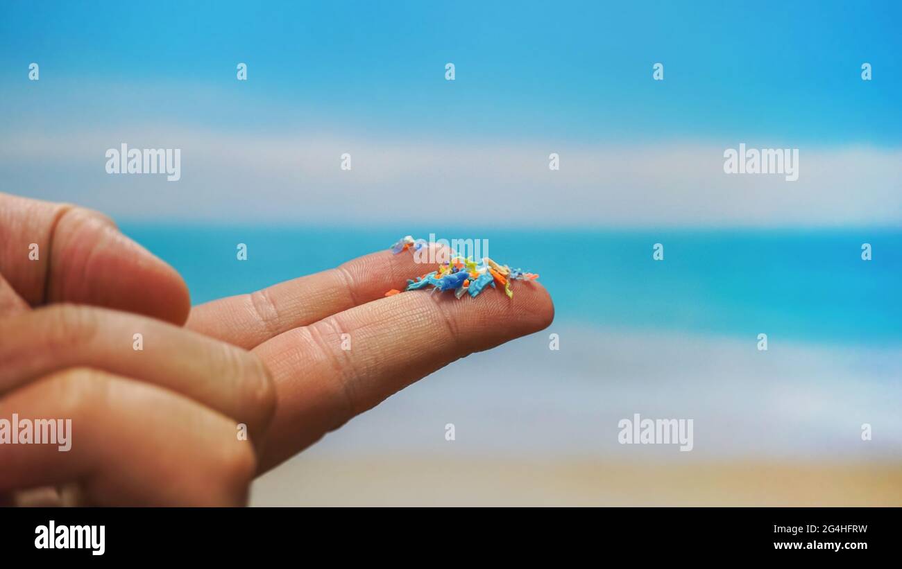 Close up side shot of microplastics on human fingers with blurred sea background. Creative concept of water pollution and global warming. Stock Photo