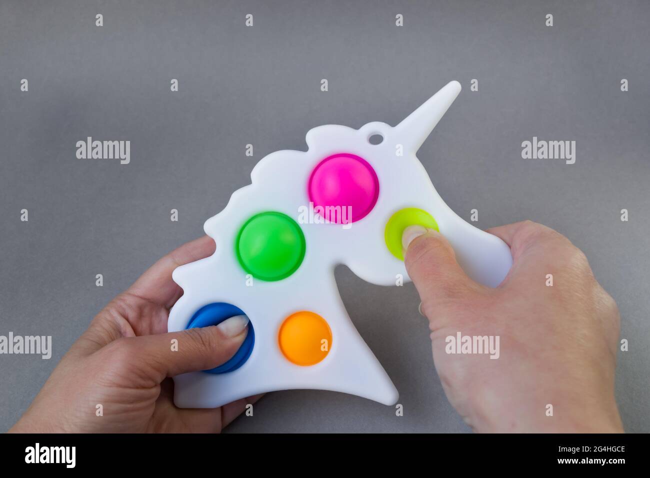 Bright colorful toy Simple Dimple unicorn. Popular anti-stress toy on a gray background in the hands of a woman Stock Photo